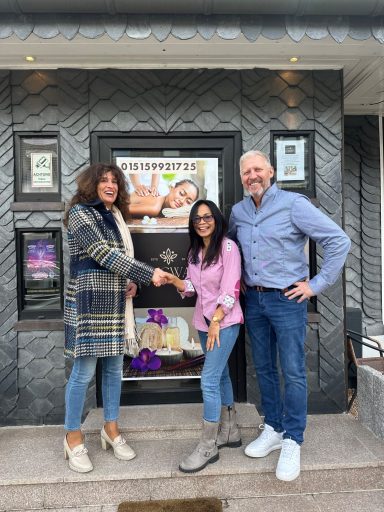 Drei Personen schütteln sich die Hände vor einem Geschäft mit Schaufensterdekoration.